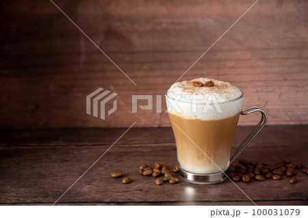 Glass cup of layered coffee drink with milk foam, wooden background and copy space 100031079