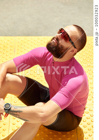 Close-up of a professional cyclist in sportswear sitting relaxing and enjoying the sun in the park, copyspace. The concept of an active and healthy lifestyle. 100032923