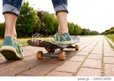 Feet on a skateboard board, rear view shot of feet with sneakers pushing a skateboard in the park, city subculture lifestyle 100033009