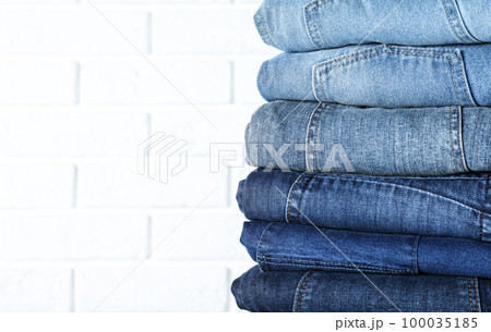 Stack of different jeans near white brick wall, closeup. Space for text 100035185