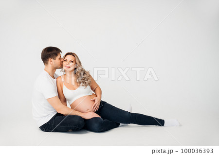 a couple waiting for a child sit on the floor of a cyclorama in a photo studio a couple waiting for a child sit on the floor of a cyclorama in a photo studio 100036393