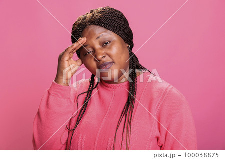 Disgusted young adult putting hand on face after smelling something stinky and disgusting in studio while posing over pink background. Displeased woman being annoying by bad smell 100038875