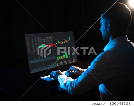 Caucasian man sits in the dark in front of a virtual screen. Stock exchange charts. Caucasian man sits in the dark in front of a virtual screen. Stock exchange charts. 100041138