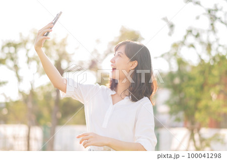 Portrait beautiful young asian woman with smart mobile phone around outdoor nature view in a sunny summer day Portrait beautiful young asian woman with smart mobile phone around outdoor nature view in a sunny summer day 100041298