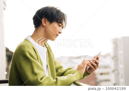 ベランダでスマホを使う男性 100042199