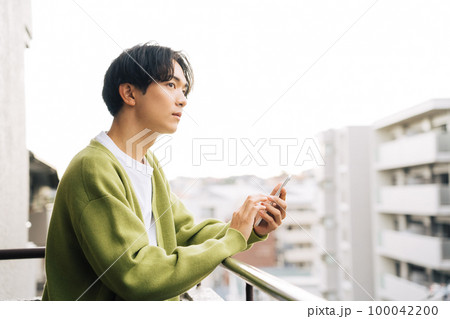 ベランダでスマホを使う男性 100042200