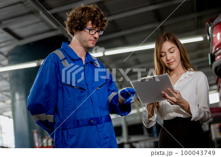 Man garage worker and woman customer talking to discuss the details of car repairs. Man garage worker and woman customer talking to discuss the details of car repairs. 100043749
