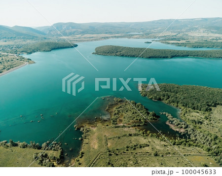 Aerial view on mountain lake. Drone over water reservoir at mountain valley covered with green spring forest. Beautiful view from above on smooth blue surface of mountain lake among highlands. Nobody Aerial view on mountain lake. Drone over water reservoir at mountain valley covered with green spring forest. Beautiful view from above on smooth blue surface of mountain lake among highlands. Nobody 100045633