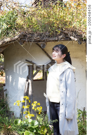 草屋根の小屋の前に立つ女性ポートレート 100048456
