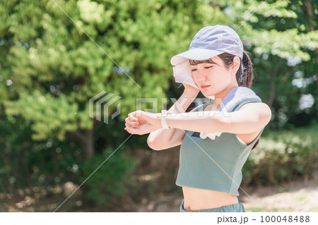 公園で腕時計を見ながら運動・トレーニング・ウォーキングする女性(時間・タイム・ヘルスケア) 100048488