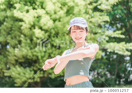 公園で運動前に日焼け止めクリームを塗る女性（紫外線対策・UVケア・スキンケア・ボディケア） 100051257