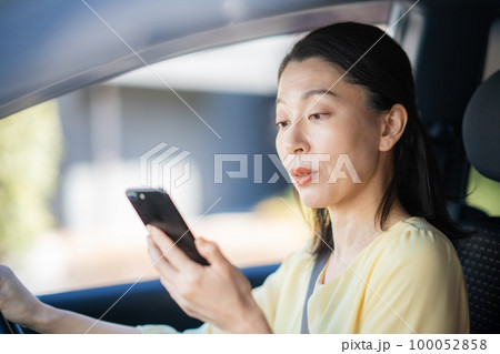 運転しながらスマホを見ているミドル女性 100052858