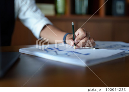 A portrait of a good-looking and discreet Asian man sitting at his desk making a thoughtful face while reading budget papers and using a computer. 100054228