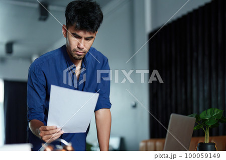 A portrait of a good-looking and discreet Asian man sitting at his desk with a thoughtful look on his computer. 100059149