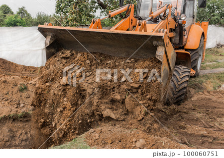 A bucket of a bulldozer fills the trench with earth in an industrial zone. Excavation construction works 100060751