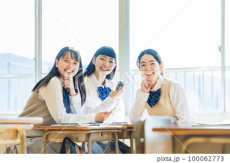 教室でクラスメイトとスマホを見ながら話す高校生 教室でクラスメイトとスマホを見ながら話す高校生 100062773