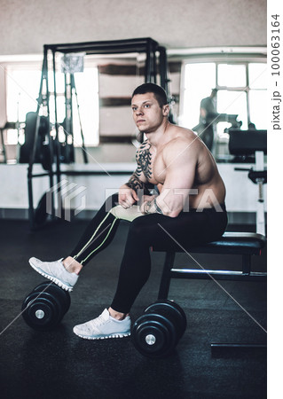 brooding male bodybuilder sitting on a bench after a workout 100063164