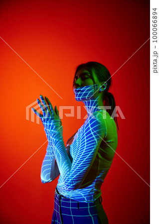 Young beautiful woman's portrait with digital neon filter lights on body over red background. Concept of art, fashion, cyberpunk, futurism and creativity 100066894