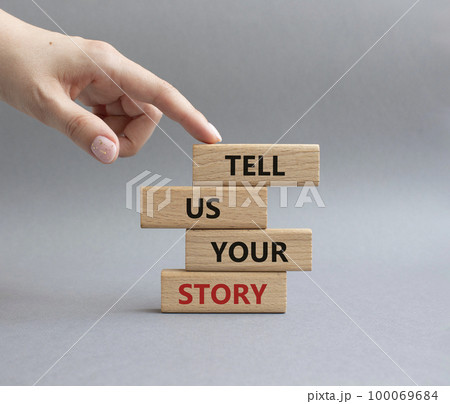 Tell us your story symbol. Concept words Tell us your story on wooden blocks. Beautiful grey background. Businessman hand. Business and Tell us your story concept. Copy space. 100069684