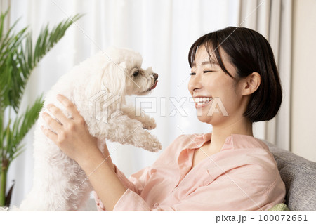 ソファーに座って笑顔で犬を抱く女性 100072661