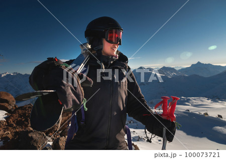 Image of a woman with skis on her shoulder against a snowy hill or mountain range. Portrait of a cheerful skier carrying skis on her shoulder Image of a woman with skis on her shoulder against a snowy hill or mountain range. Portrait of a cheerful skier carrying skis on her shoulder 100073721