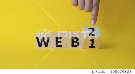 WEB 2 or 1 symbol. Businessman hand points at turned wooden cubes with words WEB 1 and WEB 2. Beautiful yellow background. Business and WEB concept. Copy space 100074328