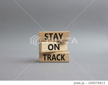 Stay on track symbol. Wooden blocks with words 'Stay on track'. Beautiful yellow background. Businessman hand. Business and 'Stay on track' concept. Copy space. Stay on track symbol. Wooden blocks with words 'Stay on track'. Beautiful yellow background. Businessman hand. Business and 'Stay on track' concept. Copy space. 100078815