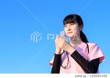 マスクを外すスクラブを着た女性看護師　医療従事者　医師　介護士　支援　医療現場　 100085206