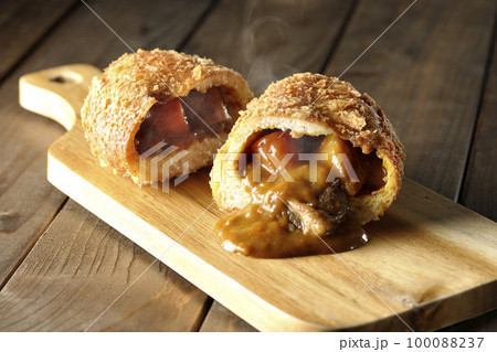 カッティングボードの上の半分にカットされルーが流れ出るゴロゴロ野菜と牛肉入り熱々カレーパン 100088237