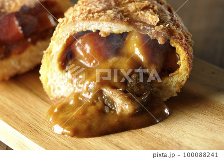カッティングボードの上の半分にカットされルーが流れ出るゴロゴロ野菜と牛肉入り熱々カレーパン カッティングボードの上の半分にカットされルーが流れ出るゴロゴロ野菜と牛肉入り熱々カレーパン 100088241