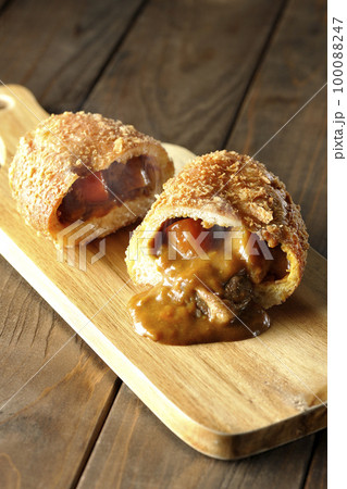 カッティングボードの上の半分にカットされルーが流れ出るゴロゴロ野菜と牛肉入り熱々カレーパン 100088247