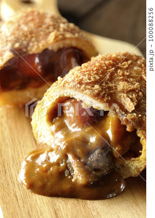 カッティングボードの上の半分にカットされルーが流れ出るゴロゴロ野菜と牛肉入り熱々カレーパン カッティングボードの上の半分にカットされルーが流れ出るゴロゴロ野菜と牛肉入り熱々カレーパン 100088256