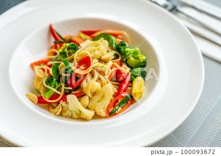 Pad Kee Mao or Thai fusion food, stirred fried spaghetti with spicy herbs, meat, and fresh vegetables. Beautiful Thai food in a white dish on a table, natural light from the window. 100093672