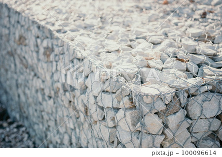 Granite stones behind a metal grate for strengthening the slope. Stones behind the wire. grey texture. construction. 100096614