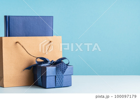 small Luxury gift box with a blue bow paper bag and agenda. Side view. Fathers day or Valentines day gift for him. Corporate gift concept or birthday party. Festive sale copy space small Luxury gift box with a blue bow paper bag and agenda. Side view. Fathers day or Valentines day gift for him. Corporate gift concept or birthday party. Festive sale copy space 100097179