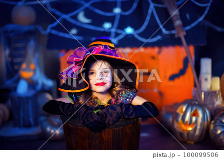Portrait of kid cute girl in witch costume peeks out of stupa on the background of halloween decor Portrait of kid cute girl in witch costume peeks out of stupa on the background of halloween decor 100099506
