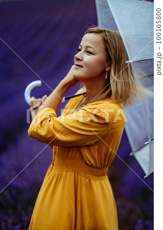 A middle-aged woman in a lavender field walks under an umbrella on a rainy day and enjoys aromatherapy. Aromatherapy concept, lavender oil, photo session in lavender A middle-aged woman in a lavender field walks under an umbrella on a rainy day and enjoys aromatherapy. Aromatherapy concept, lavender oil, photo session in lavender 100105800
