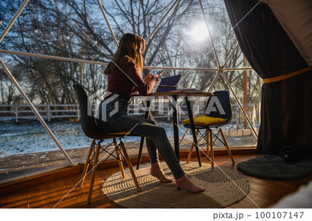 Woman sitting at a table with a phone and a laptop near the window in the hotel. 100107147