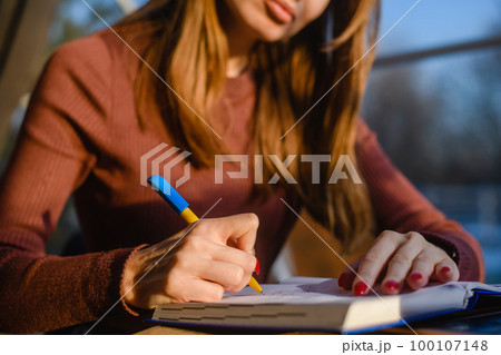 A young girl makes notes in a notebook while sitting at a table by the window. 100107148