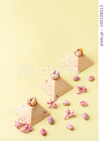 Traditional Easter cottage cheese dessert Paskha decorated with caramel and chocolate candy eggs and spring flowers on pastel yellow background. Modern minimalistic Easter background with copy space. Traditional Easter cottage cheese dessert Paskha decorated with caramel and chocolate candy eggs and spring flowers on pastel yellow background. Modern minimalistic Easter background with copy space. 100108013