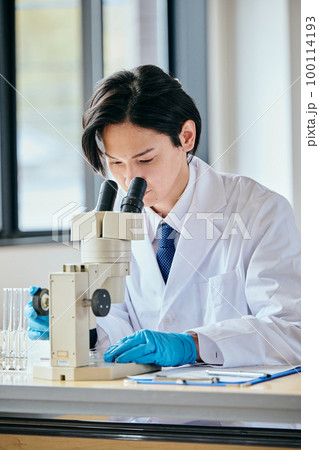 顕微鏡のレンズを覗いて観察する白衣の若い男性 100114193