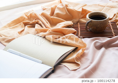 Coffee cup, bamboo tray and open notebook on bed. Good springtime morning. 100114278