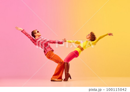 Young stylish emotional man and woman, professional dancers in retro style clothes dancing disco dance over pink-yellow background. 1970s, 1980s fashion, music concept 100115042
