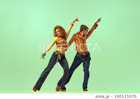 Two excited people, man and woman in retro style clothes dancing disco dance over green background. 1970s, 1980s fashion, music, hippie lifestyle, 100115070