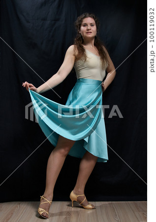 Dancing woman in a blue skirt posing against a black background. Full length portrait 100119032