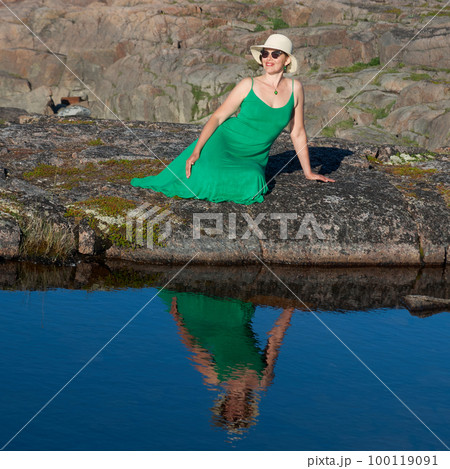 Woman tourist in a straw hat and a green dress on the seashore on a bright sunny day 100119091