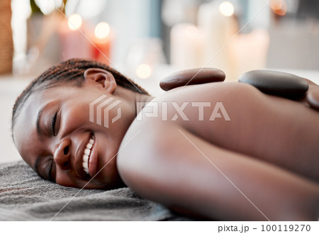 Hot stone massage, black woman at spa with smile on face, holistic healing with physical therapy and back skin detox. Happy, content and zen with wellness at luxury resort, rocks and relax with glow 100119270