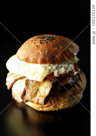 タルタルソースがはみ出てるベーコンとレタスとトマトがはさまったBLTバーガーを黒背景で撮影 100120130