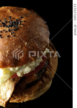 タルタルソースがはみ出てるベーコンとレタスとトマトがはさまったBLTバーガーを黒背景で俯瞰撮影 100120233