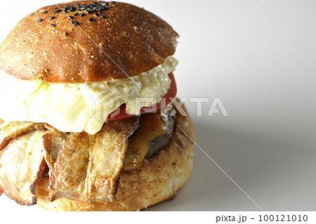 タルタルソースがはみ出ててベーコンとレタスとトマトがはさまったBLTバーガーを白背景で撮影 100121010